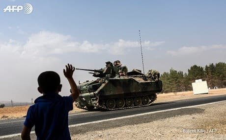 A boy waves to a Turkish tank entering Syria from the border town of Karkamis. Photo: Bulent Kilic/AFP