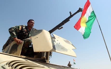 A flag of the Kurdistan Region flies next to a Kurdish peshmerga fighter as he takes position to monitor the area in Bashiqa, north-east of Mosul, in 2014. File photo: AFP/Getty Images/ Ahmad al-Rubaye