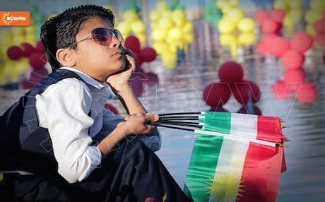 A boy holds Kurdish flags in his hand.