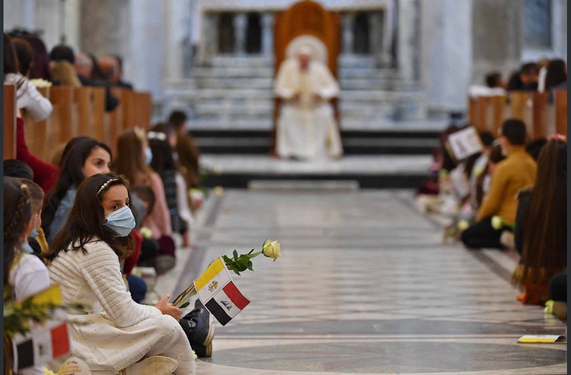  Children sit on the floor along the nave as Pope Francis (background) is seated on the throne at the Syriac Catholic Church of the Immaculate Conception (al-Tahira-l-Kubra), in the predominantly Christian town of Qaraqosh (Baghdeda), in Nineveh province, some 30 kilometres from Iraq's northern Mosul on March 7, 2021. Photo by Vincenzo PINTO / AFP