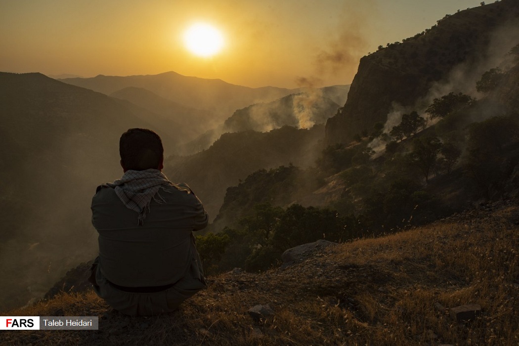 هاووڵاتییەک بە دیار دووکەڵی ئاگری دارستانەکان و ئاوابوونی خۆر دانیشتووە