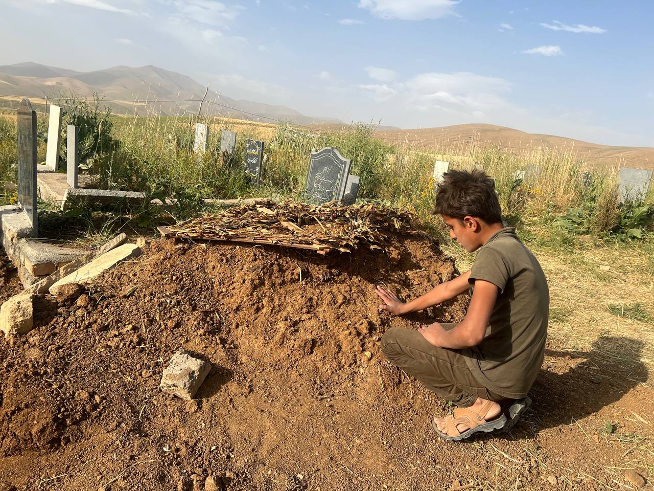 Mihran Saidanifar sits next to his father's gave in Urmia on June 22, 2022. Photo: Jabar Dastbaz/Rudaw