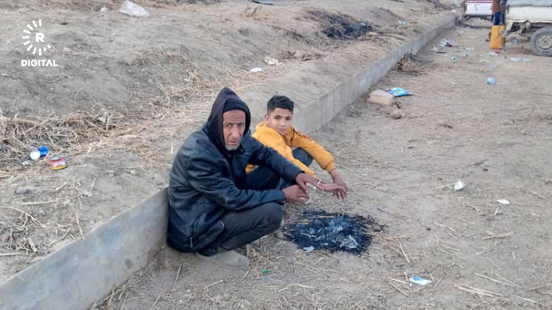 پیاوێکی بەتەمەن و منداڵێک کە لە شەهبا هەڵاتوون، لە نزیک تەبقە خۆیان لەبەر ئاگر گەرم دەکەنەوە. وێنەکە بۆ رووداو نێردراوە