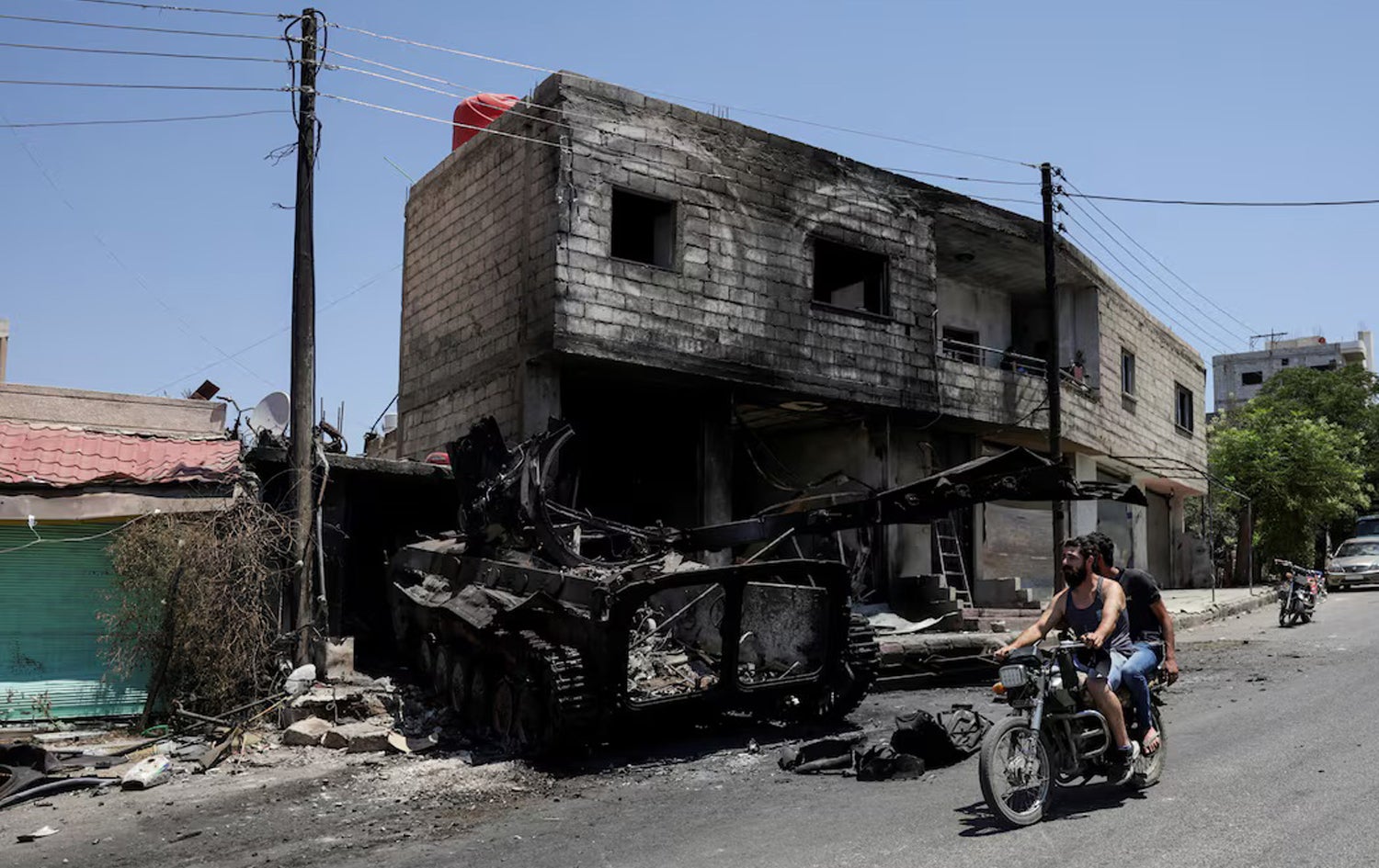 دوو کەس بە سواری ماتۆڕسکیلێکەوە لە سوەیدا بە لای تانکێکی سەربازی تەقاوە دا دەڕۆن. وێنە: Reuters