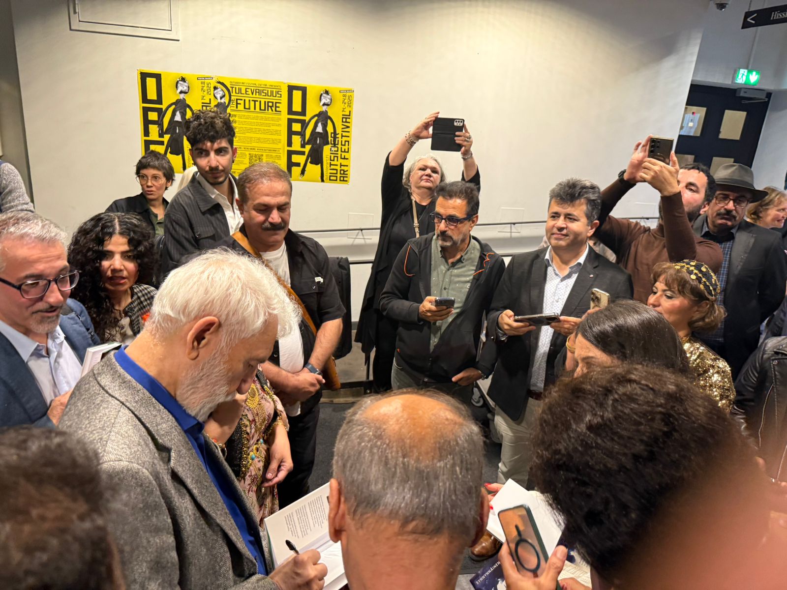 Kurdish poet Abdulla Pashew signs a book at the launch of a Finnish translation of his work in Helsinki on August 21, 2025. Photo: Rudaw