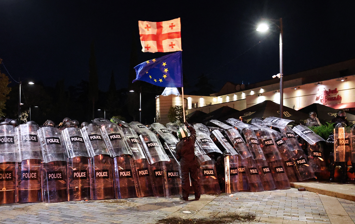 خۆپێشاندەرێک بە تەنیا لە بەرامبەر ژمارەیەکی زۆر پۆلیس وەستاوەتەوە و ئاڵای یەکێتیی ئەورووپا و وڵاتەکەی بەرزکردووەتەوە. وێنە: AFP