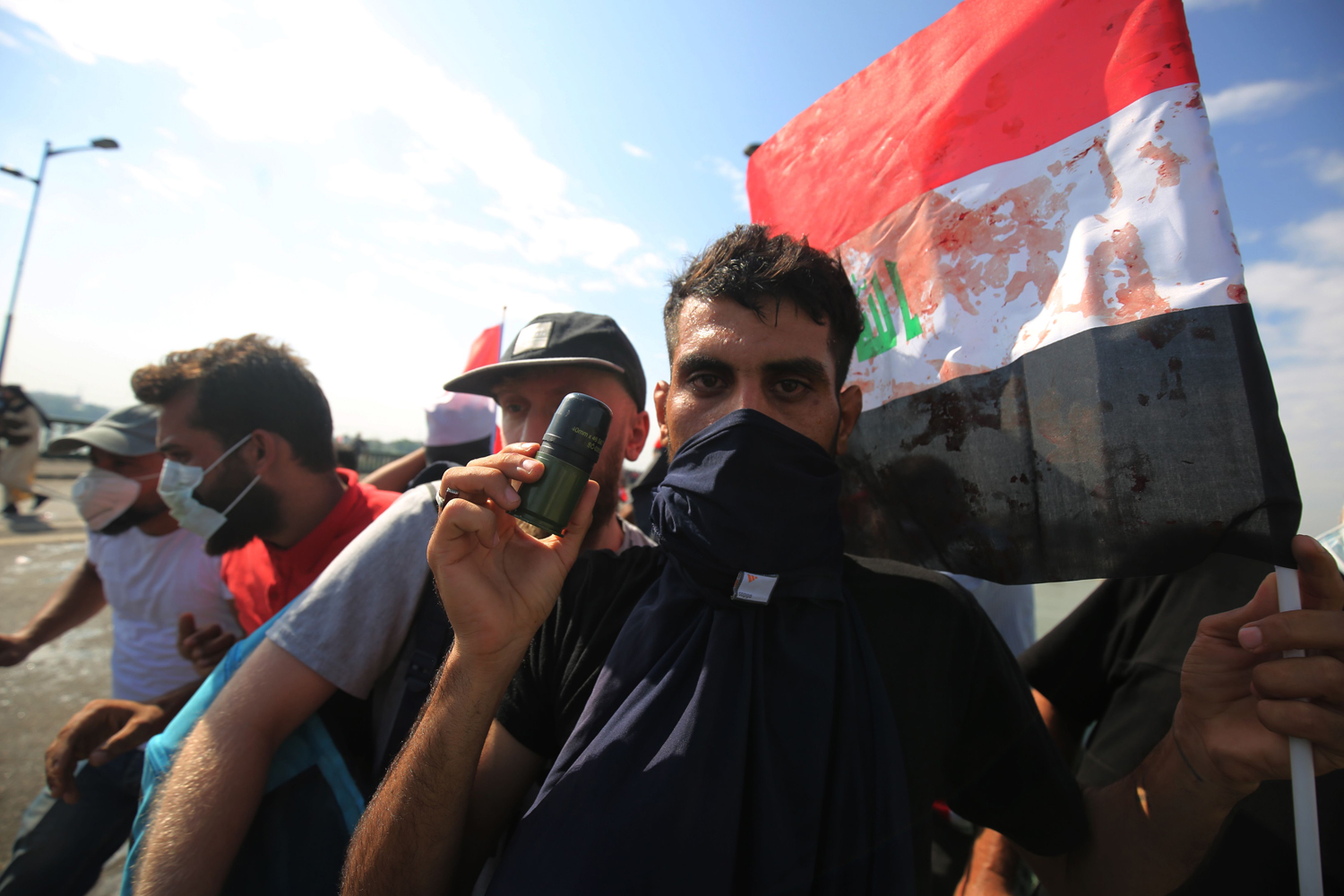 An Iraqi protestor displays an empty tear gas canister fired by security forces to disperse anti-government demonstrations and a blood-stained flag, on October 25, 2019 in Baghdad. Photo: AFP
