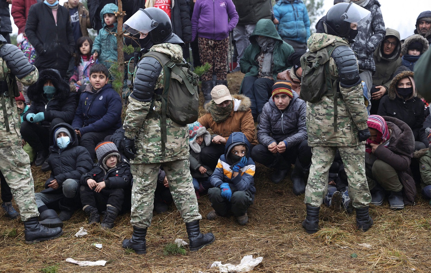 A group of migrants stands in front of Belarusian servicemen as they gather for the distribution of humanitarian aid in a camp near the Belarusian-Polish border in the Grodno region on November 14, 2021. Photo: Oksana Manchuk/BELTA/AFP
