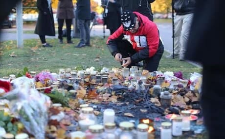 A man lights a candle outside the school in Trollhattan, a day after the attack in which two people were killed. AP photo.