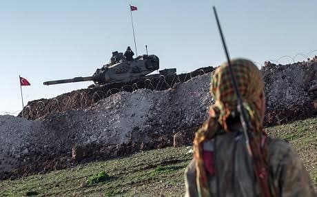 A YPG fighter eyes a Turkish tank on the Syrian-Turkish border. AP file photo.
