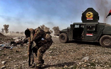 A member of Iraq's Rapid Response Unit shields himself from a blast near Mosul. Photo: Aris Messinis | AFP