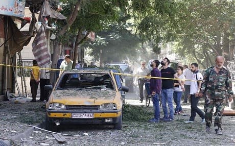 Syrians walk past charred vehicles at the site of a suicide bomb attack in the capital's eastern Tahrir Square district, on July 2, 2017. Photo: AFP / Louai Beshara