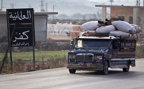 Displaced Syrians from a village in southern Idlib drive past a sign reading in Arabic: "secularism is infidelity" as they head on the Damascus-Aleppo motorway towards the northern part of the rebel-held province on December 29. Photo: Omar Haj Kadour | AFP