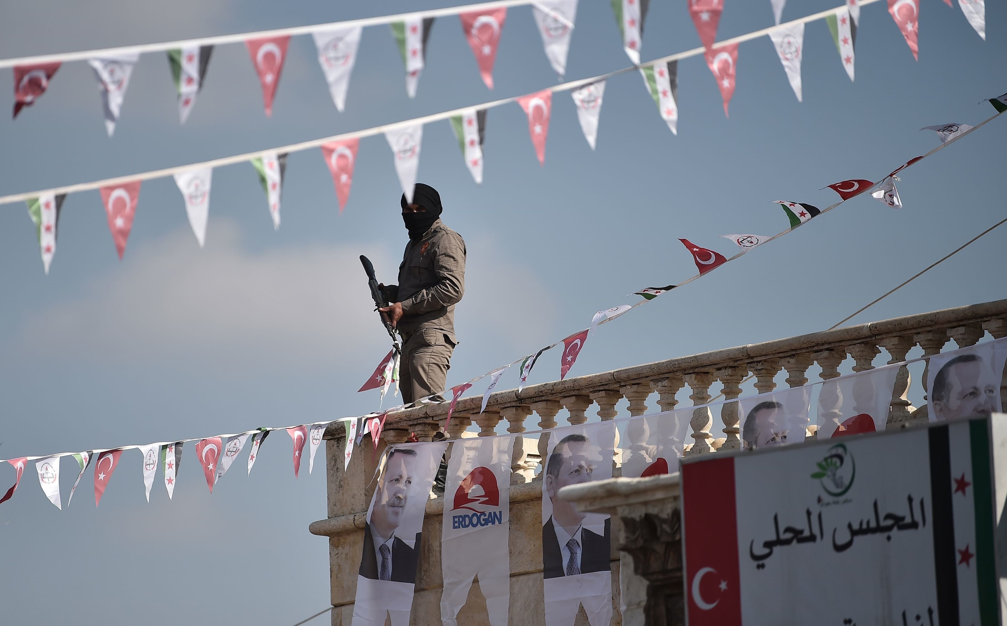 A Turkish-backed Syrian rebel fighter stands on a rooftop in Suran, Syria decorated with posters of Turkey President Recep Tayyip Erdogan last week. Photo: Ozan Kose/AFP