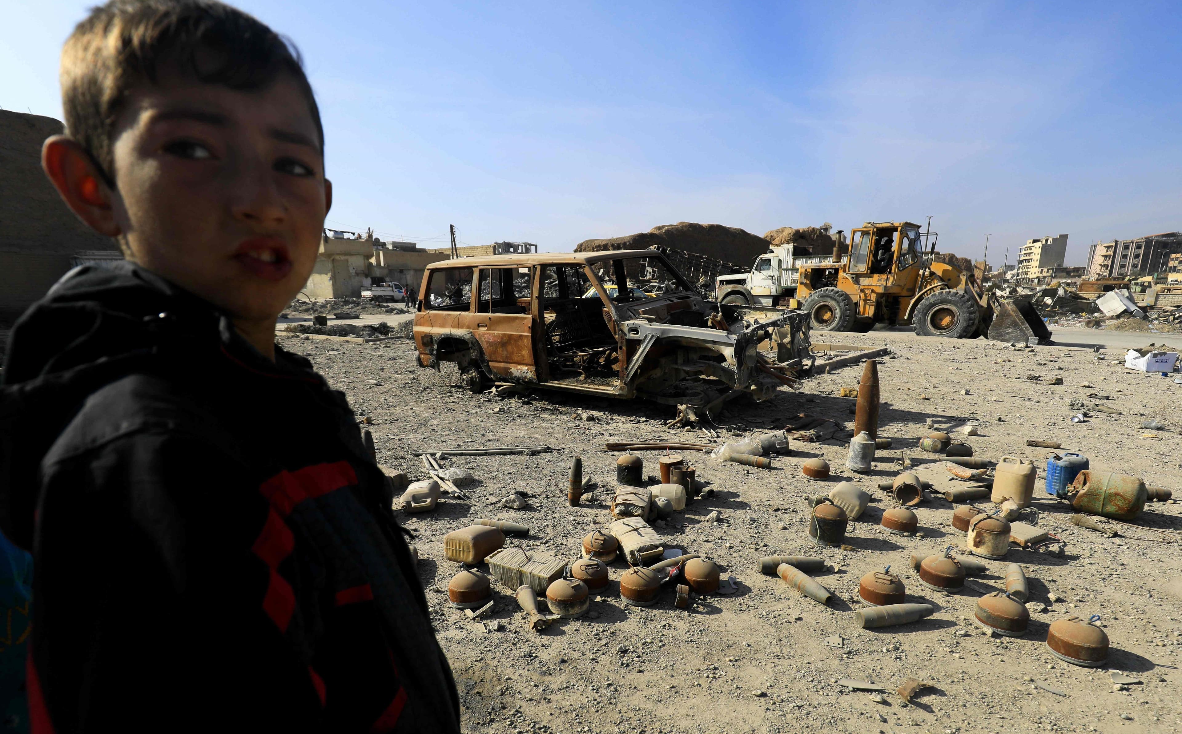 A boy stands near shells and undetonated mines lying in a Raqqa street, left behind by ISIS. Photo: Delil Souleiman/AFP