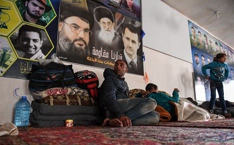 A man sits beneath posters of Syria’s Bashar al-Assad, Iranian Supreme Leader Ayatollah Ali Khamenei, and Lebanese Hezbollah leader Hassan Nasrallah on Tuesday after fleeing Afrin and taking shelter in Nubl, a northern Aleppo town under regime control. Photo: George Ourfalian/AFP