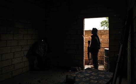 A Turkish-backed Syrian fighter peeps through a hole in a wall as another stands behind inside a building in Tadef, near the city of al-Bab, in the eastern countryside of Aleppo province on April 27, 2018. Photo: Sameer Al-Doumy | AFP