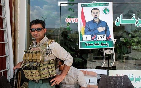 A private guard stands before a campaign poster for Rebwar Taha Mustafa, a PUK MP and candidate in oil-rich Kirkuk, on April 30, 2018. Photo: Sabah Arar | AFP