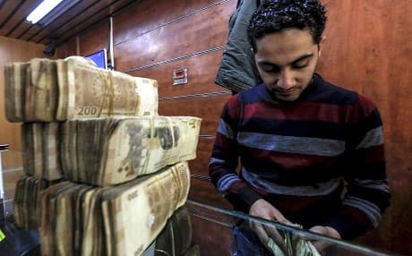 An employee of a currency exchange counter counts banknotes at a market street in Qamishli, Rojava. Photo: Delil Souleiman/AFP