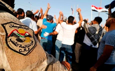 A member of the Iraqi anti-riot police stands guard as dozens shout slogans and wave national flags during a demonstration outside the local government headquarters in the southern city of Basra on Friday. Photo: Haidar Mohammed Ali/AFP