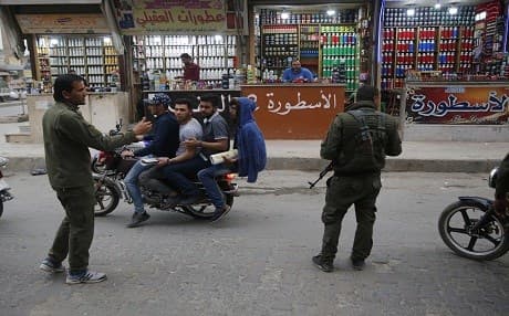 In this March 28, 2018 file photo, Syrians ride a motorcycle as they pass a checkpoint of the Kurdish internal security forces, in Manbij, north Syria. AP Photo/Hussein Malla