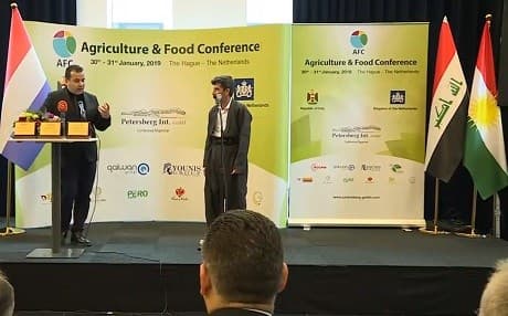 Famed Kurdish farmer Azad Mohammed speaks onstage at the Agriculture and Food Conference in The Hague on January 31, 2019, framed by the (L to R) Dutch, Iraqi, Kurdistan flags. Photo: Rudaw