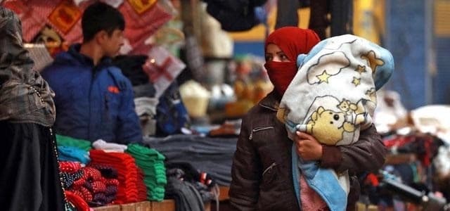A woman carries a child along a market alley in the northeastern Syrian city of Qamishli. File photo: AFP 
