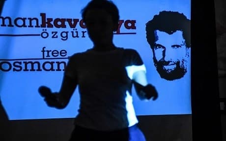 In this file photo taken on October 31, 2018 a woman passes in front of a screen featuring jailed businessman and philanthropist Osman Kavala during a press conference of his lawyers. Photo: Ozan Kose | AFP