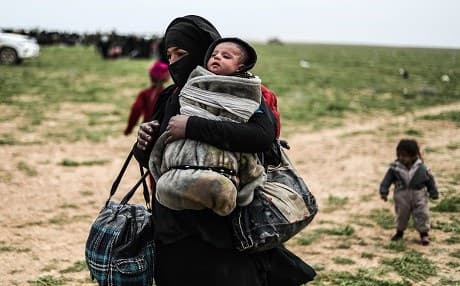 A woman flees the ISIS holdout of al-Baghouz while carrying a baby and walking toward US-backed SDF positions in al-Baghouz, Syria, on February 26, 2019. Photo: Delil Souleiman | AFP
