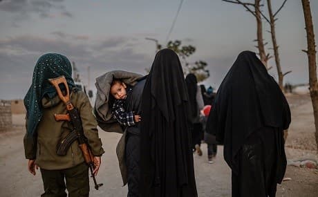 Veiled women, reportedly wives and members of the Islamic State, walk under the supervision of a female fighter from the Syrian Democratic Forces (SDF) at al-Hol camp in Hasaka, northeastern Syria, February 17, 2019. Photo: Bulent Kilic / AFP