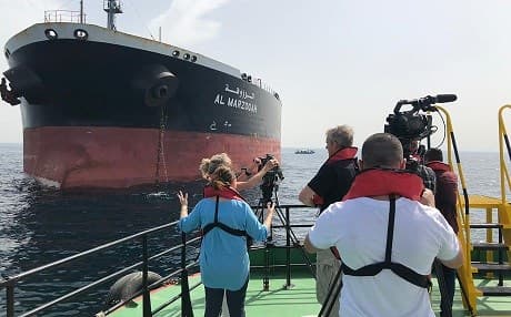 A picture taken on May 13, 2019 off the coast of the Gulf emirate of Fujairah shows reporters taking images of the Saudi oil tanker Al-Marzoqah, one of the four tankers damaged in alleged "sabotage attacks" in the Gulf the previous day. Photo: handout/Emirati National Media Council/AFP