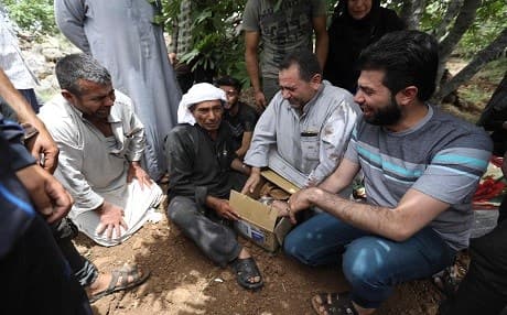 A group of mourners gather around a carboard box containing the remains of a child killed in an aerial bombardment in northern Idlib province before the victim's burial on June 5, 2019, on the outskirts of the village of Kafr Aweid. Photo: Omar Haj Kadour | AFP