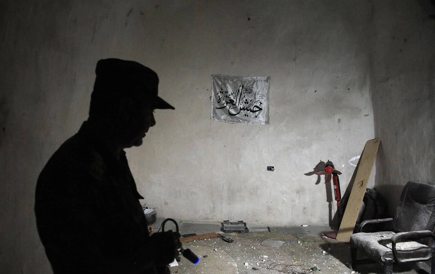 A Syrian army officer stands in a room that is part of a cave and tunnel system reportedly used by anti-government fighters, with the flag of Jaysh al-Izza (Army of Glory) seen hanging on a wall, near al-Lataminah in Hama province, September 25, 2019. Photo: Maxime Popov / AFP 