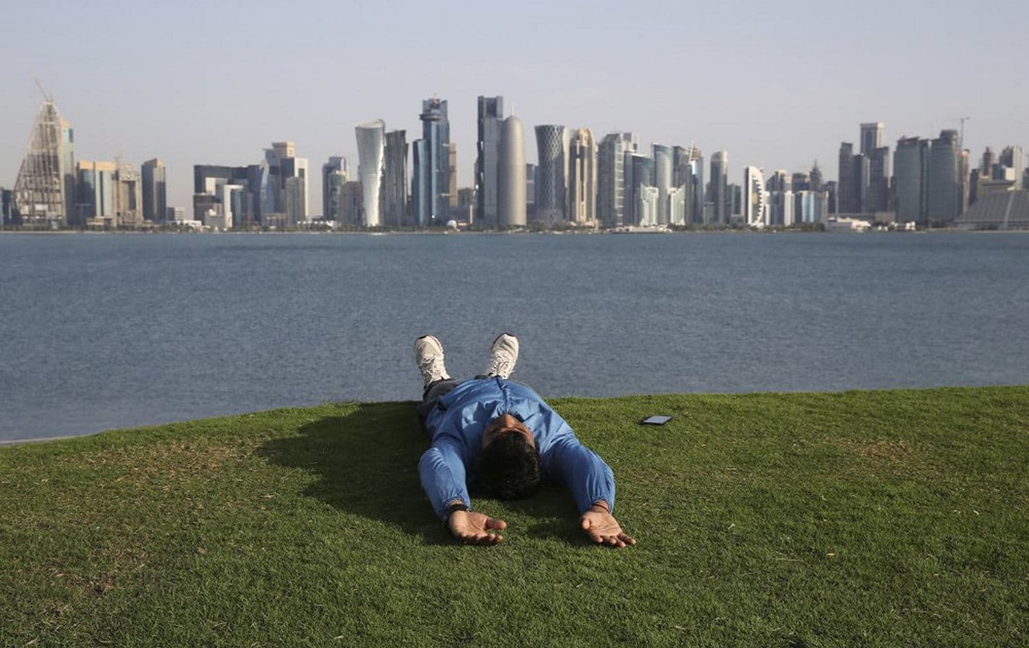 A man lies on a grass-covered hill at MIA park overlooking the skyline of Doha, Qatar, April 19, 2019. File photo: Kamran Jebreili / AP 