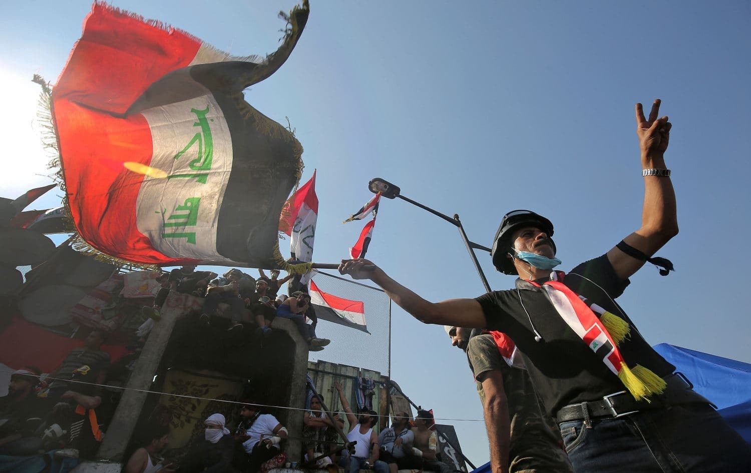 An Iraqi demonstrator waving a national flag flashes the victory sign near al-Jumhuriya bridge which leads to the high-security Green Zone, during ongoing anti-government protests in Baghdad on November 4, 2019. Photo: AFP / Ahmad al-Rubaye