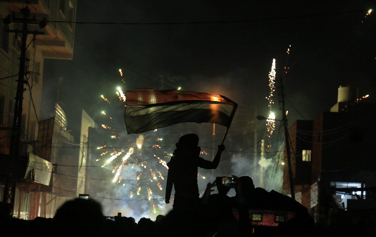 An Iraqi demonstrator waving the national flag is silhouetted during clashes with security forces in Karbala on November 29, 2019,. Photo: Mohammed Sawaf/AFP
