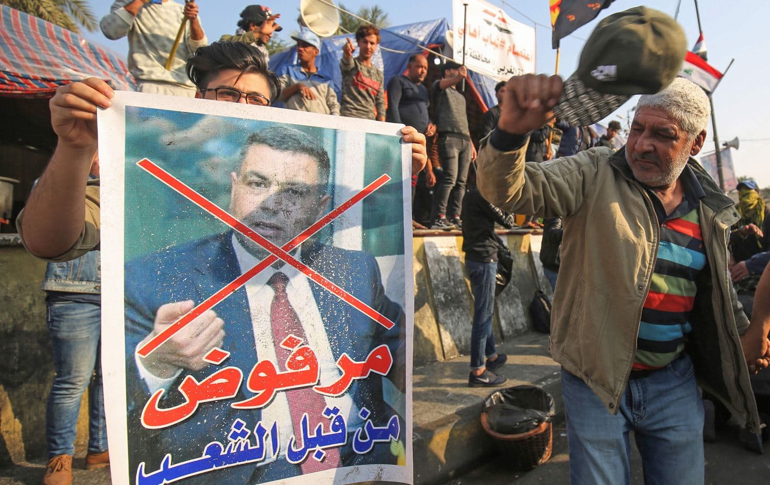 An Iraqi anti-government protester beats with his cap a defaced poster of Assaad al-Aidani, the governor of Basra, during a demonstration in Baghdad's Tahrir Square on December 26, 2019. Photo:  AFP / Ahmad Al-Rubaye