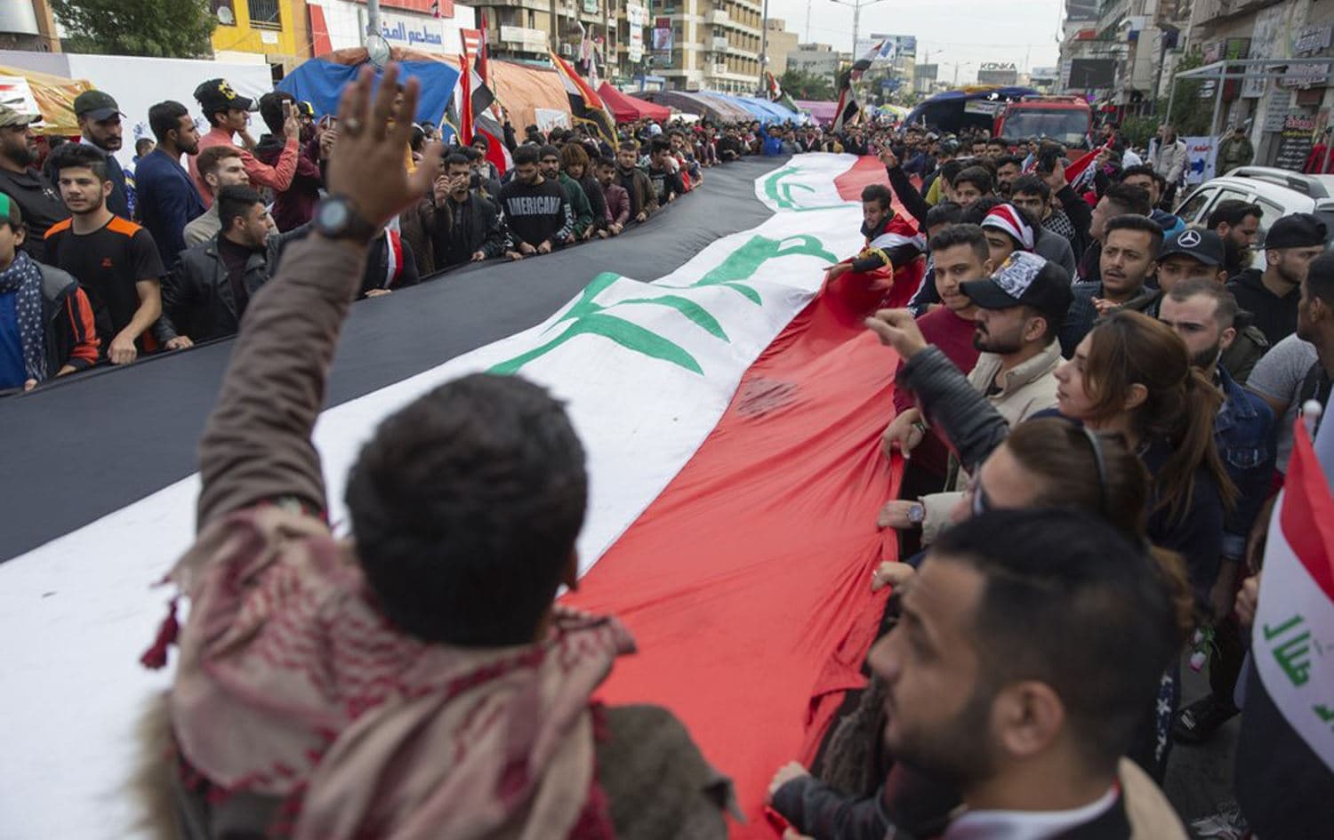 Anti government protesters carry a big Iraqi flag and chant anti Iran and anti U.S. slogans during the ongoing protests in Tahrir square, Baghdad, Iraq, Friday, Jan. 10, 2020. Photo: AP/ Nasser Nasser