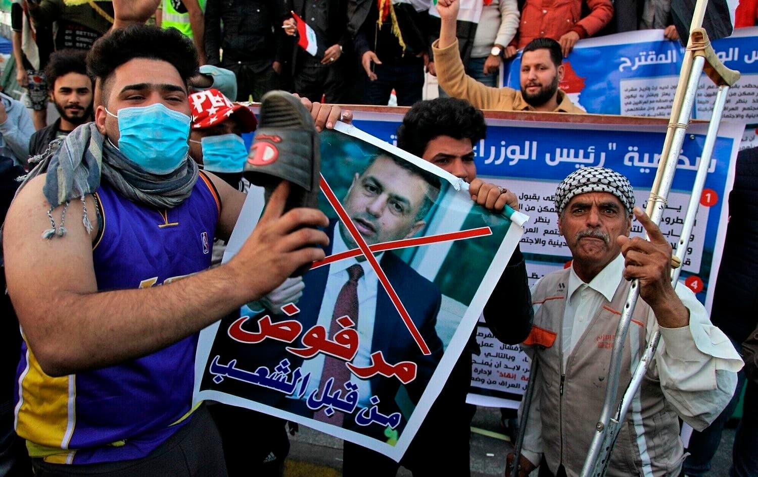 A protester hits a poster with a defaced picture of Assaad al-Aidani, the Iran-backed parliamentary bloc's nominee for PM with a shoe in Baghdad on December 26, 2019. Photo: Khalid Mohammed/AP 