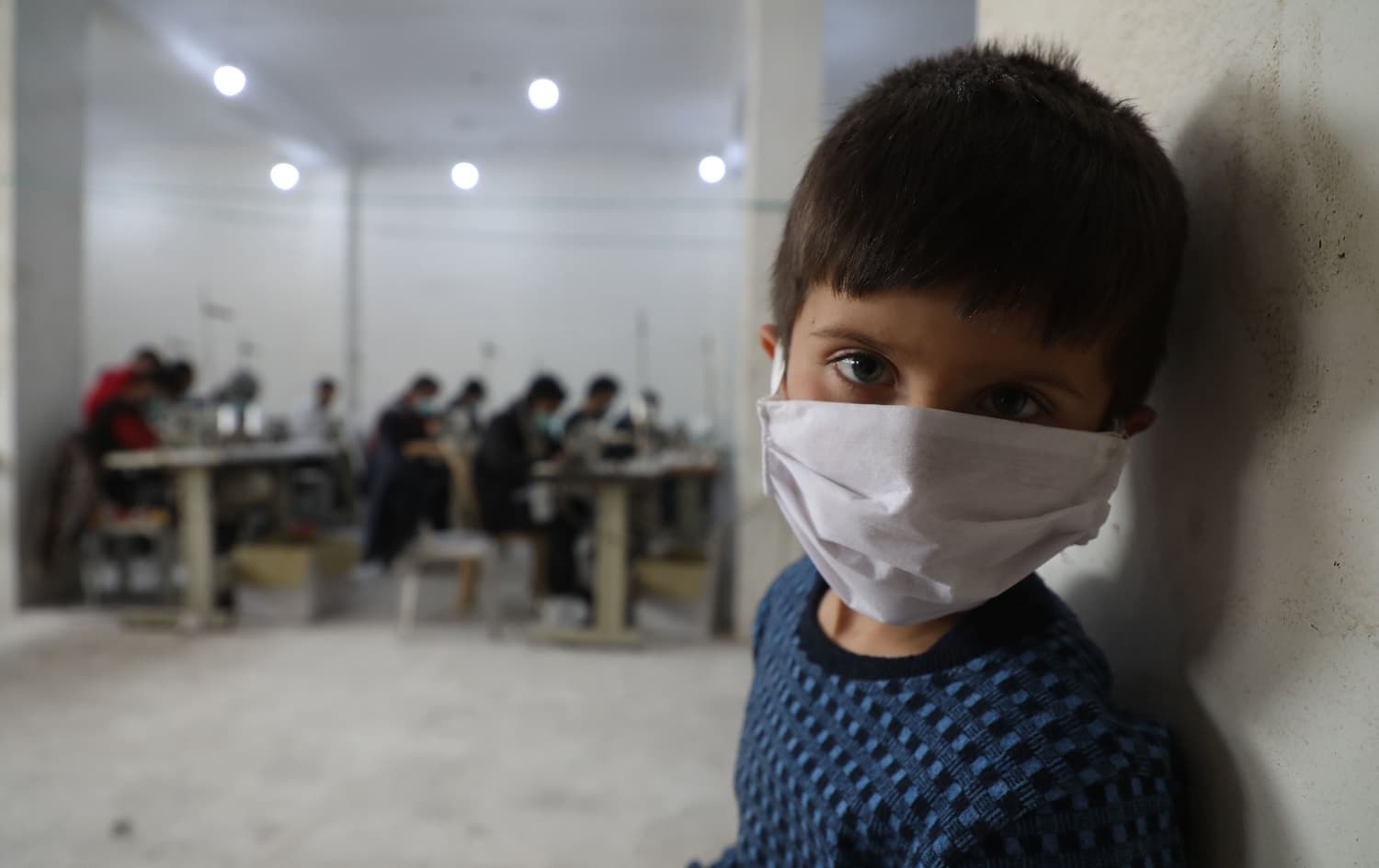 A child looks on as volunteers gather in a sewing workshop to make protective face-masks in the northeastern Syrian city of Idlib, March 28, 2020. File photo: Aaref Watad / AFP