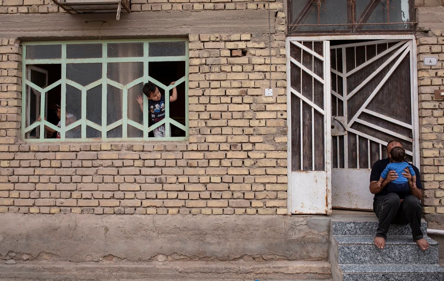 An Iraqi boy looks out of his window at a neighbour sitting with a child on the porch, amid confinement due to the COVID-19 pandemic, in the southern city of Basra, on April 25, 2020. Hussein Faleh/ AFP