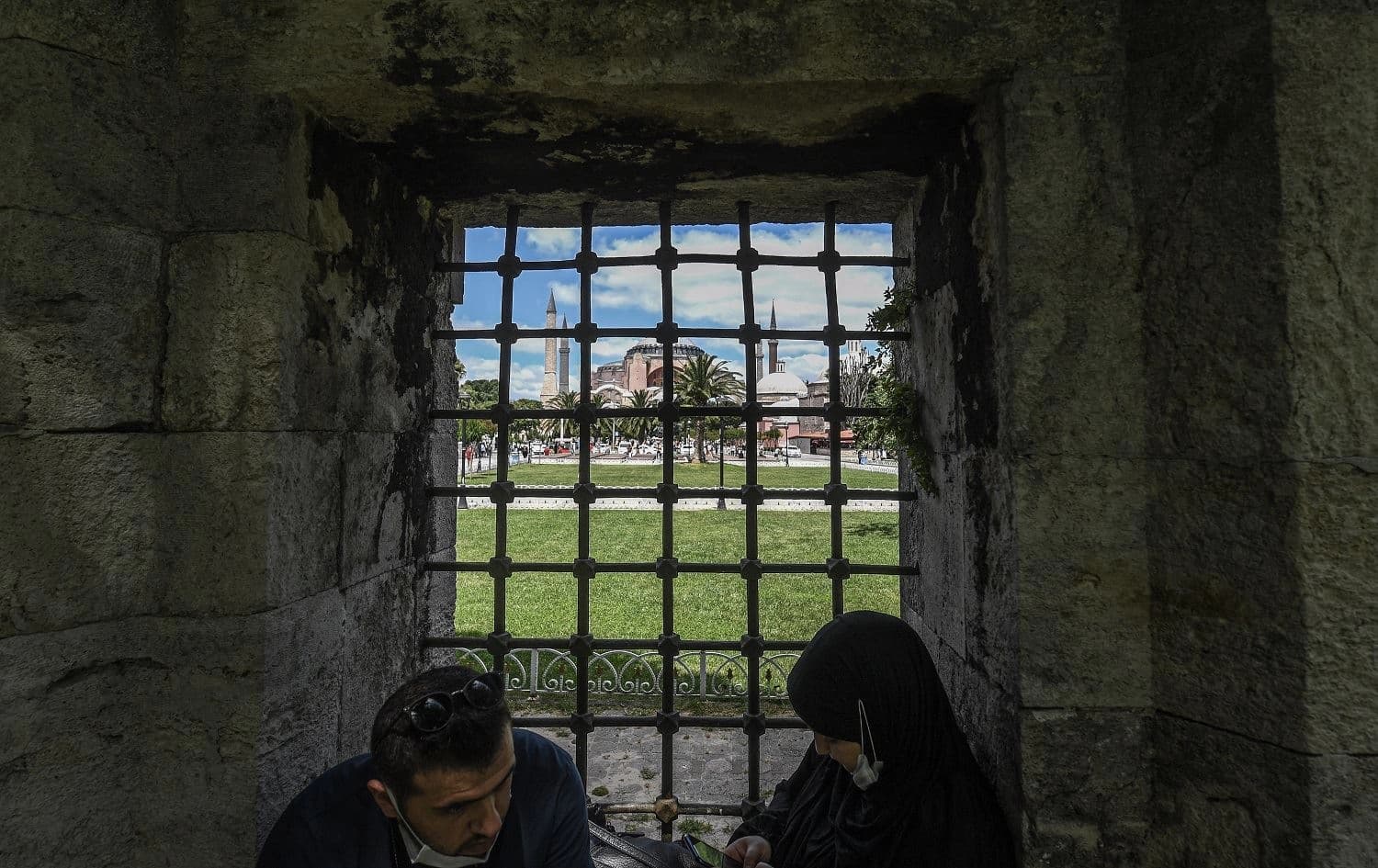Two person are sitting in the garden of Sultanahmet mosque as Hagia Sophia is seen in the backround on July 11, 2020 in Istanbul. Photo: Ozan Kose / AFP