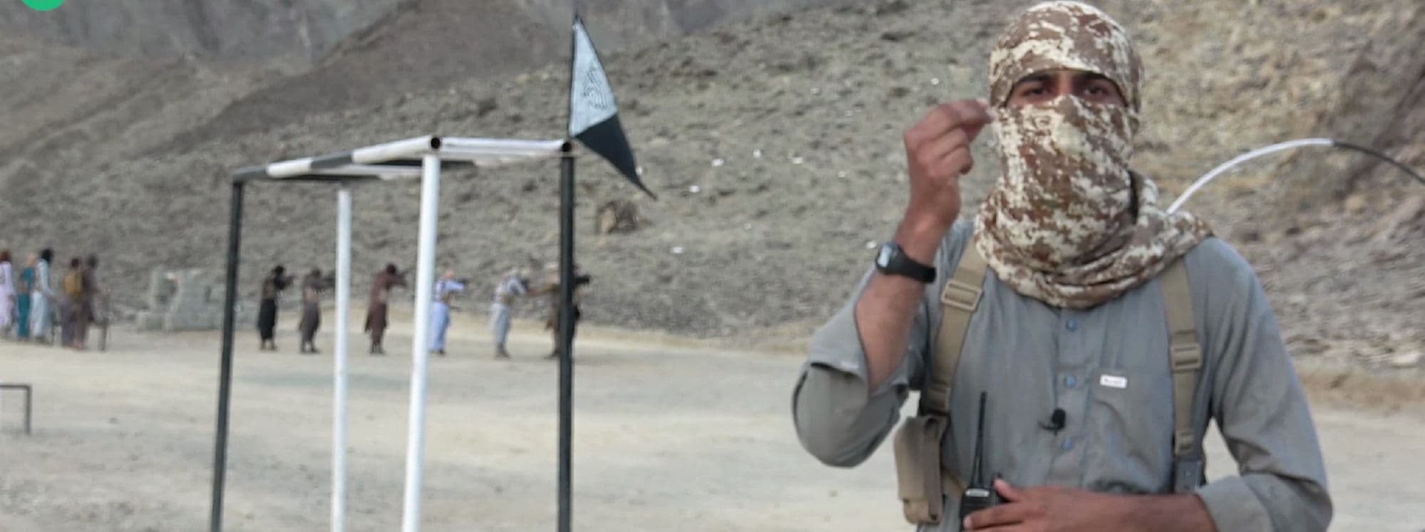 a Jaish al-Adl fighter speaks to the camera as a number of other fighters train in the background. Photo: Telegram