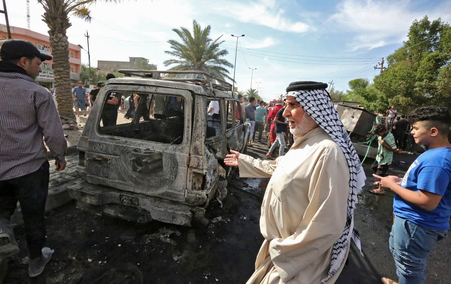 People gather around a destroyed vehicle at the scene of an explosion in the al-Habibiya district of Baghdad's Sadr City suburb on April 15, 2021. Photo: Sabah Arar/AFP