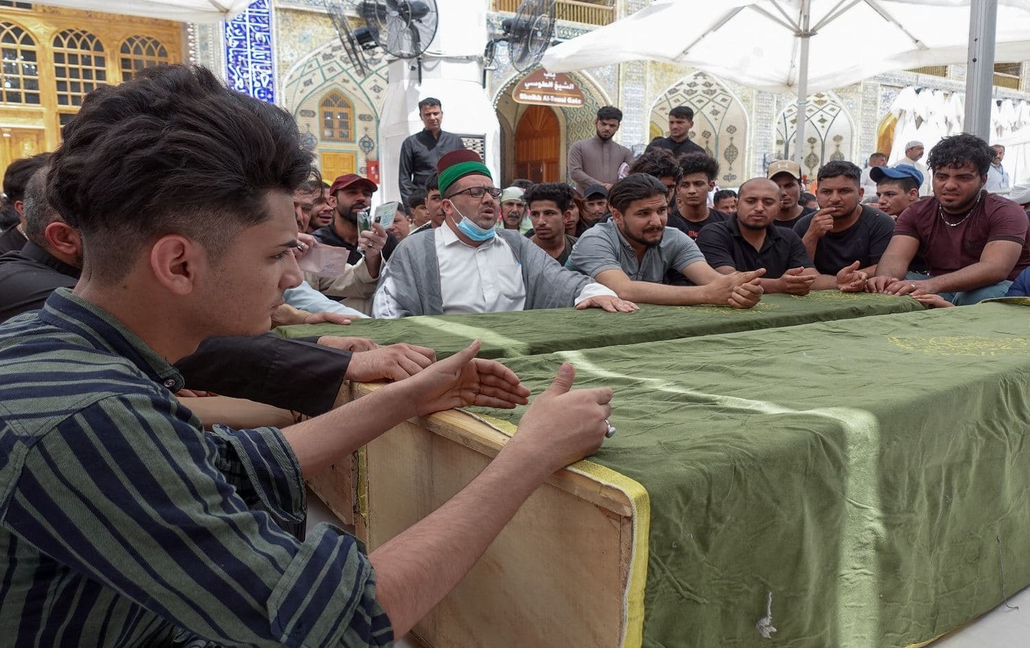 Iraqi mourners pray by coffins of relatives killed during a fire in a hospital in the capital, during a funeral procession at the Imam Ali shrine in the holy city of Najaf, on April 25, 2021. Photo: Ali Najafi / AFP