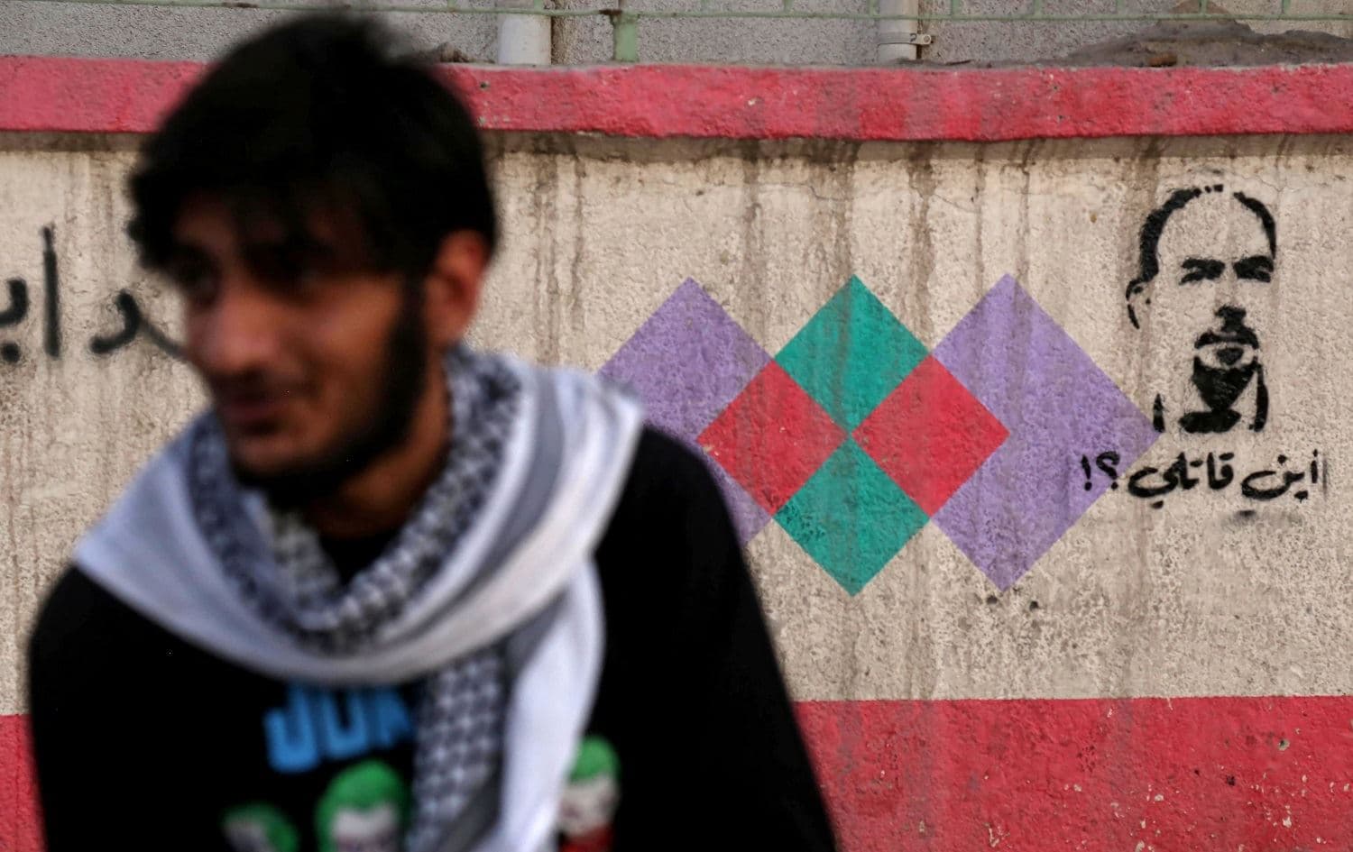 An Iraqi sits in front of graffiti in Karbala on May 23, 2021 reading in Arabic "Where's my killer?" and depicting anti-government activist Ihab al-Wazni who was shot dead earlier this month. Photo: Mohammed Sawaf/AFP