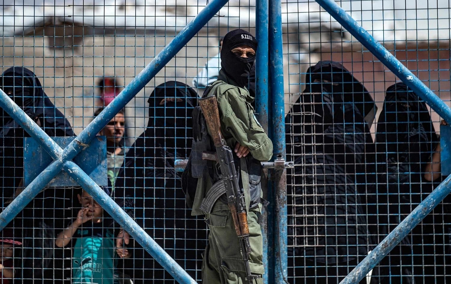A fighter from the Syrian Democratic Forces (SDF) guards a gate as Syrian women wait inside the Kurdish-run al-Hol camp in Rojava on July 15, 2021. Photo: Delil Souleiman/AFP