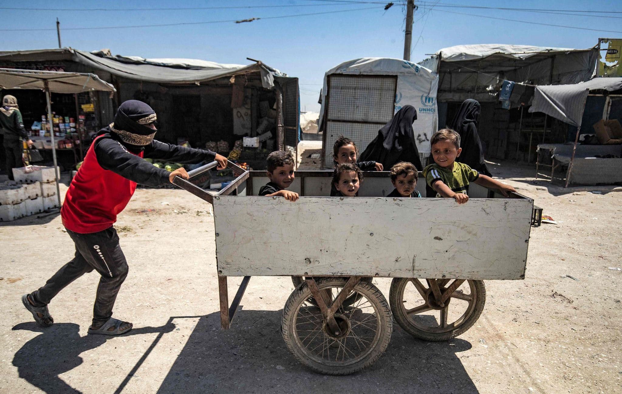A man pushes a cart with children seated inside at al-Hol camp on June 26, 2021. Photo: Delil Souleiman / AFP