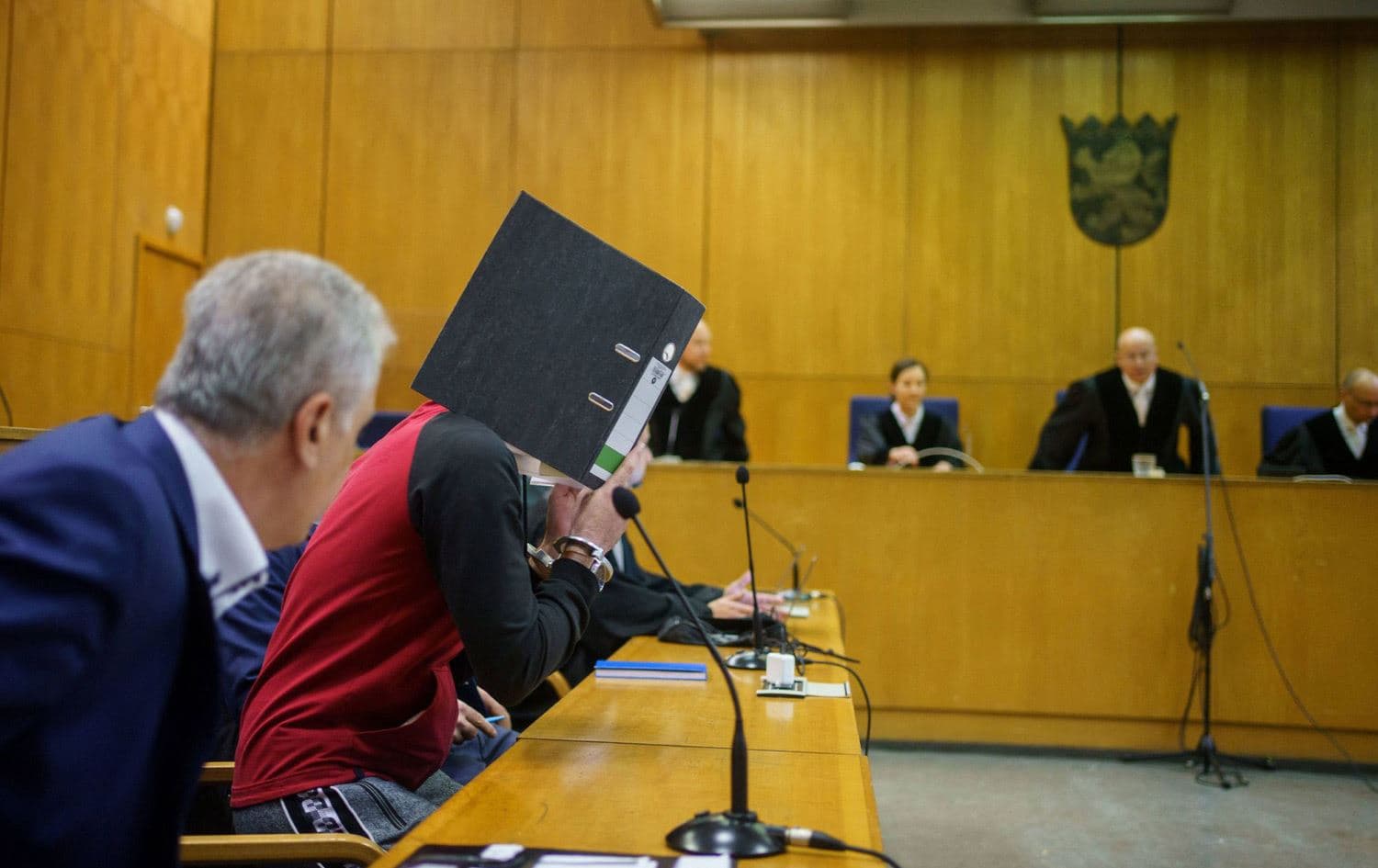 Taha Al-Jumailly holds up a file to cover his face during his trial at the Higher Regional Court in Frankfurt, Germany. Date: November 30, 2021. Photo: AFP