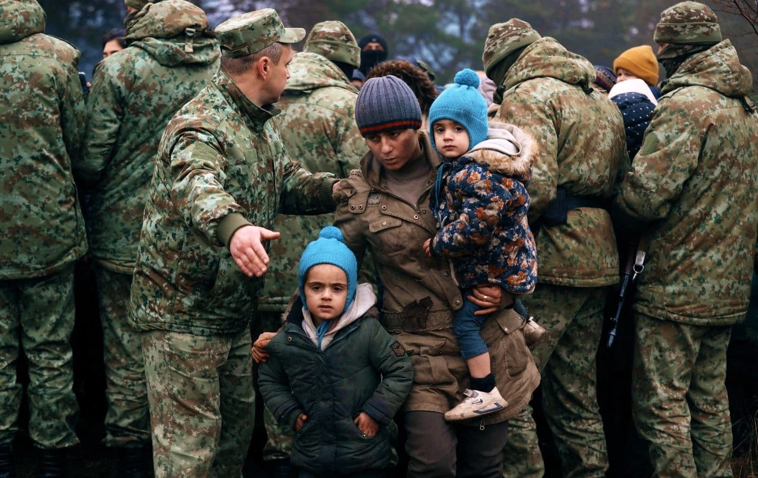 A family stands in front of Belarusian servicemen on the Belarus-side of the Belarus-Poland border on November 14, 2021. Photo: Photo: Oksana Manchuk/ AFP